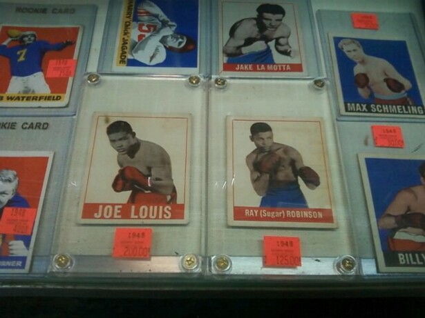 Image description: trading cards featuring white and black boxers and football players in plastic holders fill a display case. 