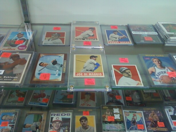 Image description: approximately 26 baseball and basketball cards featuring white and black baseball players in plastic holders fill a display case.