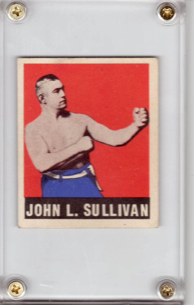 Image description: a 1948 Leaf Boxing John L. Sullivan trading card, in a plastic holder with gold screws. Boxer John L. Sullivan, a shirtless white man wearing blue pants with a white belt, assumes a boxing stance against a red background with a white border. Below him, "JOHN L. SULLIVAN" is printed in white letters on a black background.