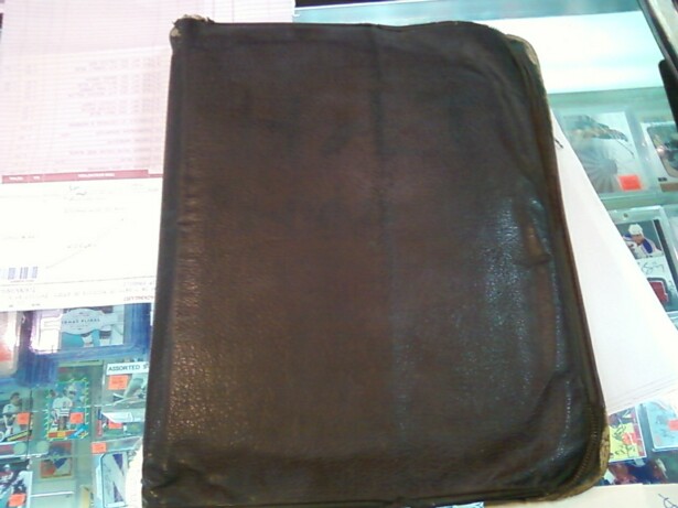 Image description: an old, worn brown leather scrapbook, center, sits on top of a glass display case filled with trading cards.