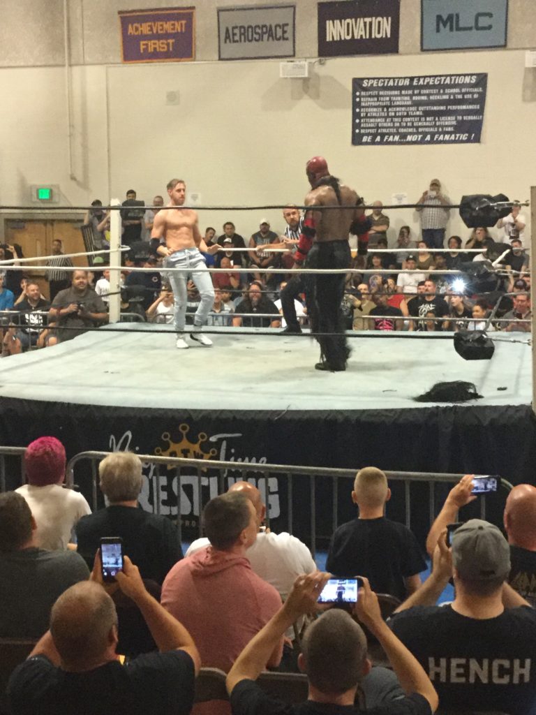 Orange Cassidy (left, a shirtless man in blue jeans with reddish blonde hair and white skin) faces The Boogeyman (right, a shirtless man with brown skin, head painted red, wearing black pants) as the crowd looks on at a Blitzkrieg Pro/Big Time Wrestling event, August 24th, 2019.