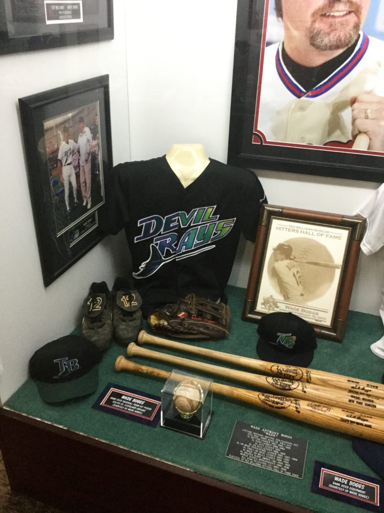 Wade Boggs' case in the Hitters Hall of Fame section of the Ted Williams Museum, located at Tropicana Field in St. Petersburg, Florida. A Devil Rays jersey, several baseball bats, 2 baseball caps, a glove, a baseball, and several pictures and plaques are visible in the case.