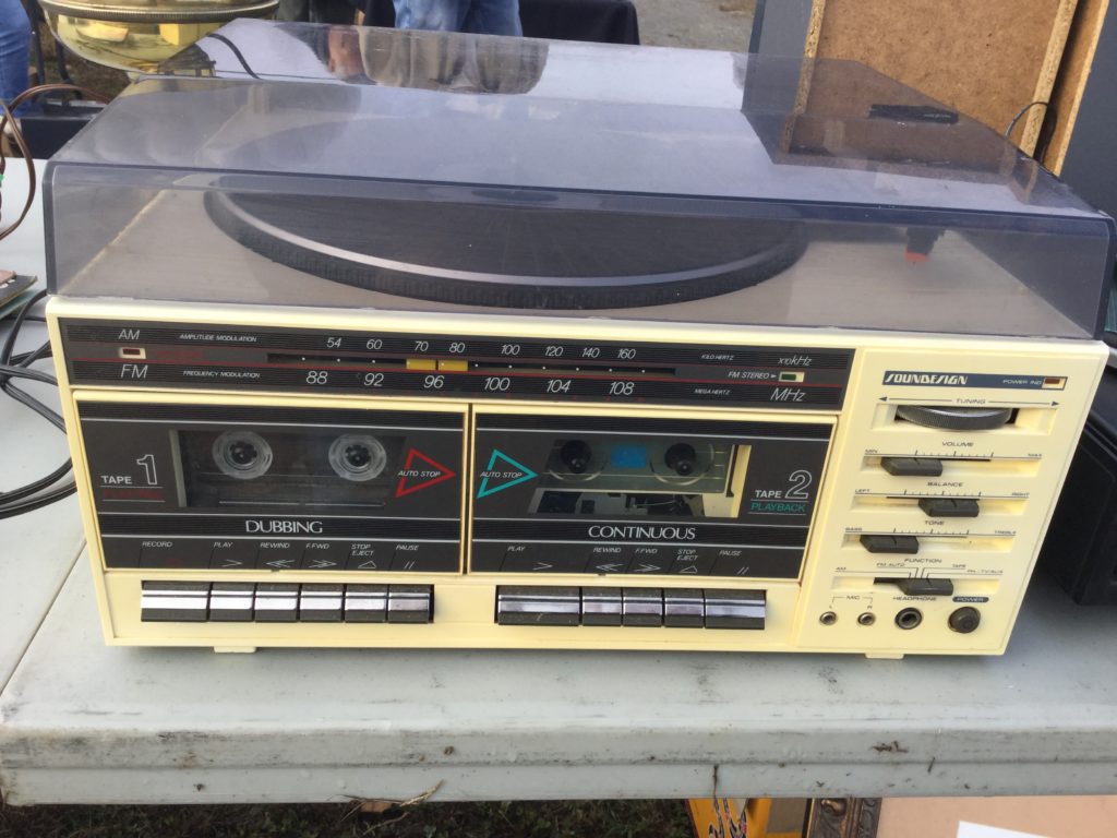 A beige 1980s-era Soundesign stereo system sits on a flea market table.