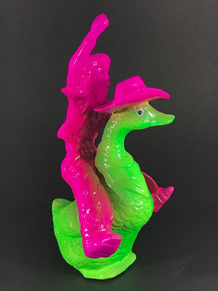 A ceramic sculpture of a neon green duck wearing a neon pink cowboy hat, with a neon pink cowboy riding it, his fist raised triumphantly.