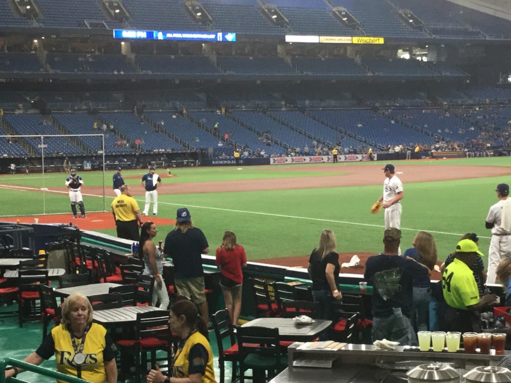 Tampa Bay Rays pitcher Brendan McKay warms up in the bullpen of Tropicana Field. Just in front of the bullpen, fans and Rays staff circulate in the picnic area of the ballpark.