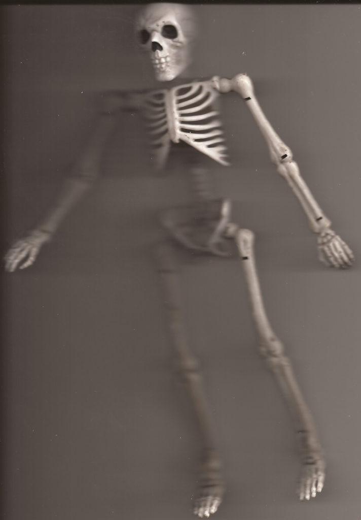 a plastic and rubber bendable action figure of a white skeleton lays on a scanner bed.